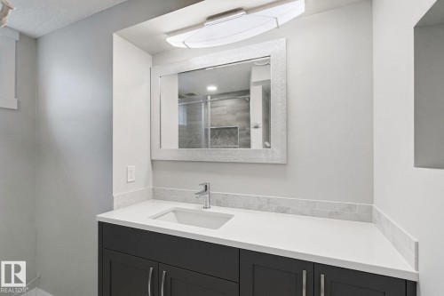 Vanity featuring a white countertop with an integrated sink, polished chrome faucet, and dark wood-finish cabinetry - 13212 73 Street Nw, Edmonton, AB 