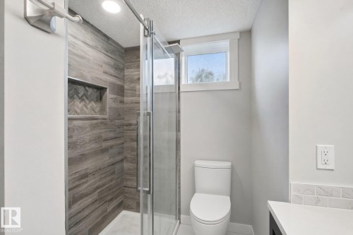 Glass-enclosed shower with wood-look tile, recessed niche featuring a herringbone pattern, and a single window - 13212 73 Street Nw, Edmonton, AB 