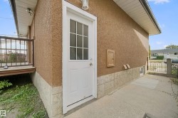 White paneled door with windowpanes, stucco exterior, stone-look foundation, concrete pathway, and a wood deck with dark railing - 