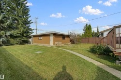 Expansive grassy yard featuring a concrete pathway, detached auxiliary building, wood privacy fencing, and mature trees - 