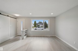 Laminate wood-finish flooring, recessed lighting, large window, white trim, and a white barn door - 