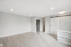 Wood-finish flooring, recessed lighting, and a white barn door with black hardware - 