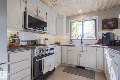 White painted cabinetry with black hardware, stainless steel range with microwave, subway tile backsplash, dark countertops, and wood-finish ceiling - 2 Hillview Crescent, Sherwood Park, AB 