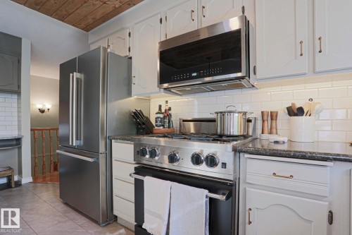 Stainless steel appliances, subway tile backsplash, light-toned cabinetry, dark countertops, and wood-paneled ceiling - 2 Hillview Crescent, Sherwood Park, AB 