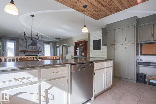 Kitchen island with stone countertop, integrated dishwasher, and white cabinetry - 2 Hillview Crescent, Sherwood Park, AB 