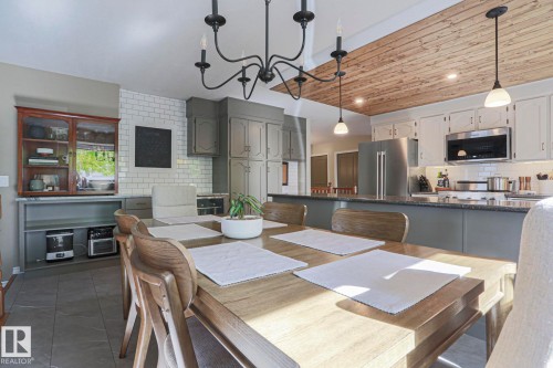Integrated dining area with chandelier lighting and wood-finish ceiling, featuring a kitchen with stainless steel appliances, subway tile backsplash, and dark countertops - 2 Hillview Crescent, Sherwood Park, AB 
