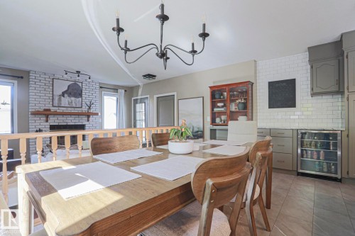 Exposed brick fireplace with a wood mantel, light wood-tone flooring, light grey cabinetry, subway tile backsplash, and a built-in beverage refrigerator - 2 Hillview Crescent, Sherwood Park, AB 