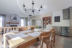 Exposed brick fireplace with a wood mantel, light wood-tone flooring, light grey cabinetry, subway tile backsplash, and a built-in beverage refrigerator - 