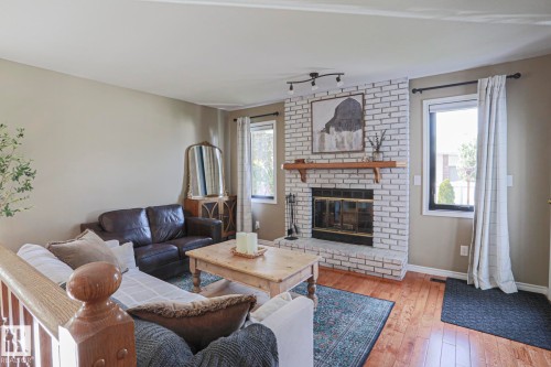Living space featuring a whitewashed brick fireplace with a wood mantel, rich wood-finish flooring, and multiple windows - 2 Hillview Crescent, Sherwood Park, AB 