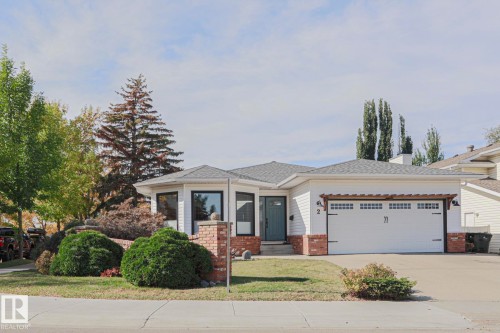 White siding exterior with brick accents, black-framed windows, an attached two-car garage, and a landscaped front yard with mature shrubbery - 2 Hillview Crescent, Sherwood Park, AB 