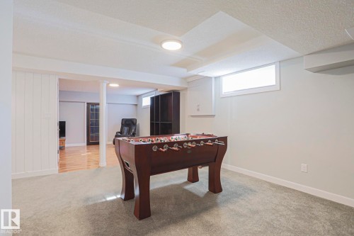 Carpeted recreation room featuring natural light, white trim, and a built-in storage cabinet - 2 Hillview Crescent, Sherwood Park, AB 