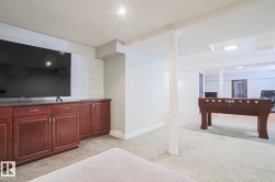 Recessed lighting, wood-finish cabinetry, built-in media console with dark countertop, carpet flooring, and white shiplap accent wall - 