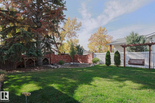Expansive lawn area, framed by mature trees, a brick retaining wall, and a white panel fence - 2 Hillview Crescent, Sherwood Park, AB 