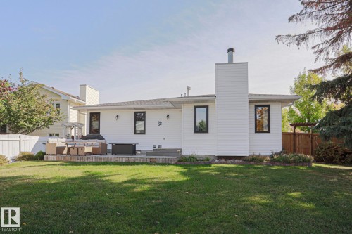 Expansive backyard featuring a manicured lawn, a large wood-finish patio, and a white privacy fence - 2 Hillview Crescent, Sherwood Park, AB 
