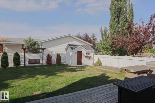Expansive backyard featuring a lush lawn, white privacy fencing, a wood pergola with a swing, and a storage shed - 2 Hillview Crescent, Sherwood Park, AB 