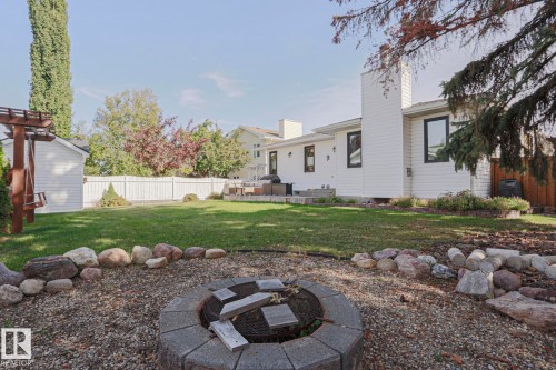 Expansive backyard featuring a stone-lined fire pit, manicured lawn, white privacy fencing, and a separate storage shed - 2 Hillview Crescent, Sherwood Park, AB 