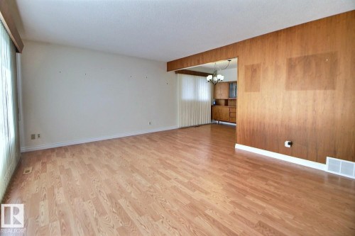 Wood-finish flooring throughout, with a wood-paneled accent wall, and an expansive window with vertical blinds - 4420 117A Street Nw, Edmonton, AB 