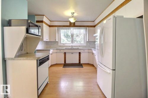 White cabinetry with integrated appliances, light-toned flooring, and a window above the sink - 4420 117A Street Nw, Edmonton, AB 