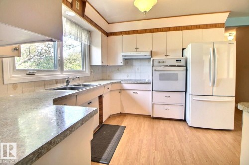 U-shaped kitchen featuring wood-finish flooring, white cabinetry, integrated double basin sink, and built-in oven - 4420 117A Street Nw, Edmonton, AB 