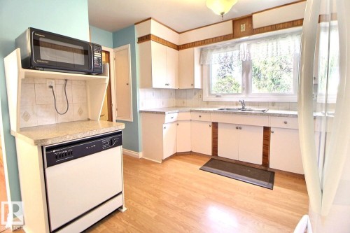 Wood-finish flooring, white cabinetry, integrated dishwasher, and a double-basin stainless steel sink - 4420 117A Street Nw, Edmonton, AB 