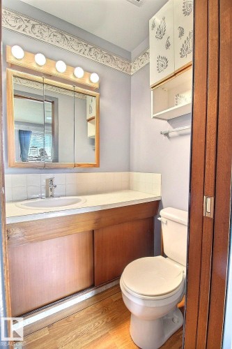 Bathroom featuring a built-in vanity with an integrated sink, wood-finish flooring, a wall-mounted medicine cabinet, and overhead lighting fixture - 4420 117A Street Nw, Edmonton, AB 