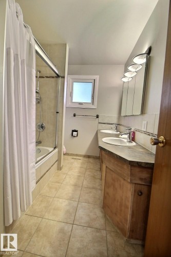 Tiled flooring, double vanity with dual sinks, built-in wooden cabinetry, mirrored medicine cabinet, and a window for natural light - 4420 117A Street Nw, Edmonton, AB 