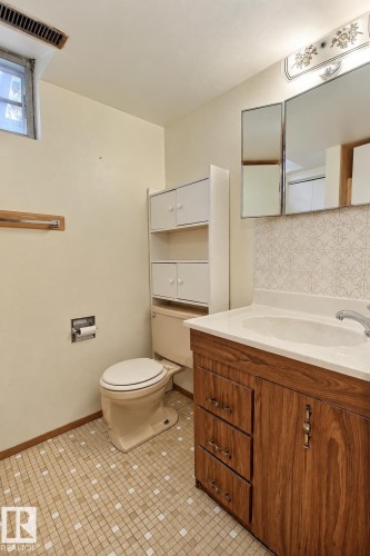 Wood-finish vanity with a single basin sink, mosaic tile flooring, and integrated wall cabinetry - 4420 117A Street Nw, Edmonton, AB 