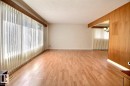 Expansive room featuring wood-finish flooring, large windows, and a wood-paneled accent wall - 4420 117A Street Nw, Edmonton, AB 