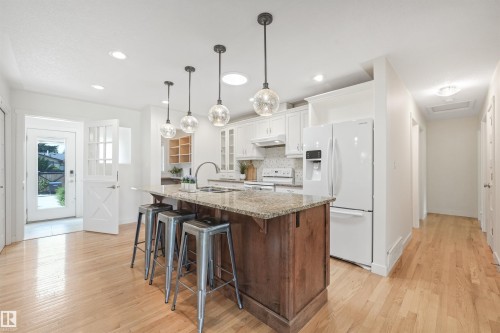 Kitchen featuring a wood-finish island with a stone-finish countertop, stainless steel sink, white cabinetry, and recessed lighting - 8212 148 Street Nw, Edmonton, AB 