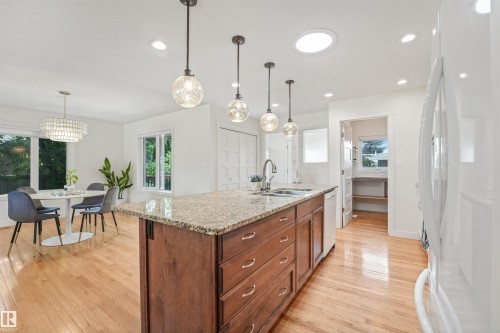 Open-concept kitchen with wood-finish flooring, a central island featuring a stone countertop, and pendant lighting - 8212 148 Street Nw, Edmonton, AB 