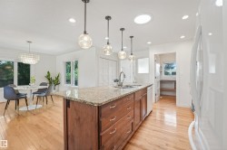 Open-concept kitchen with wood-finish flooring, a central island featuring a stone countertop, and pendant lighting - 