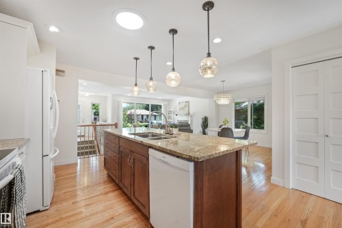 Light wood-finish flooring throughout, kitchen island with granite countertop, stainless steel double basin sink, and pendant lighting - 8212 148 Street Nw, Edmonton, AB 