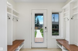Entryway featuring built-in white cabinetry, integrated wood-finish benches, and dark metal coat hooks - 