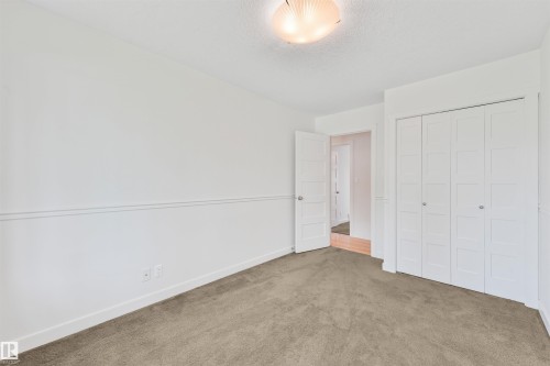 Neutral carpeted flooring, white walls, decorative wall molding, white bi-fold closet doors, and an overhead flush-mount light fixture - 8212 148 Street Nw, Edmonton, AB 
