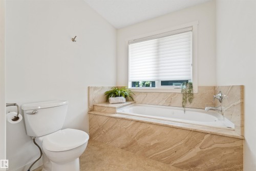 Built-in soaking tub with a tiled surround, chrome fixtures, and a white toilet - 8212 148 Street Nw, Edmonton, AB 