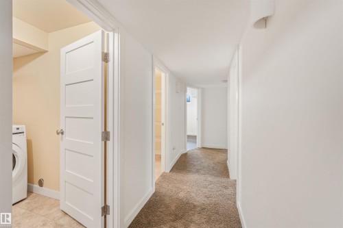Hallway with carpet flooring, white walls, recessed lighting, and a visible laundry area with tile flooring and a built-in washer - 8212 148 Street Nw, Edmonton, AB 