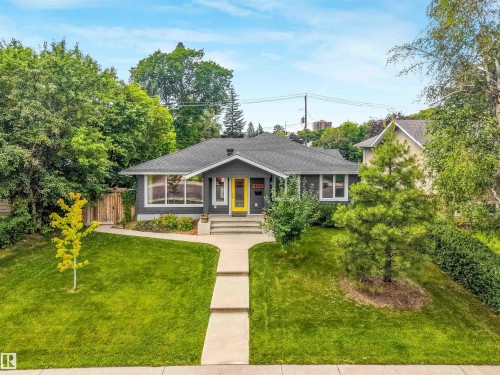 Charcoal gray siding with white trim, a bold yellow front door, a sloped shingle roof, a concrete walkway, and a landscaped front yard - 8212 148 Street Nw, Edmonton, AB 