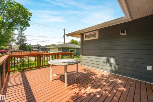Expansive wood-finish deck with wood railings and black spindles, featuring a dark gray siding exterior - 8212 148 Street Nw, Edmonton, AB 