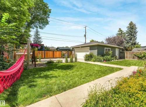 Detached garage with a white overhead door, concrete pathway, and landscaped garden beds - 8212 148 Street Nw, Edmonton, AB 