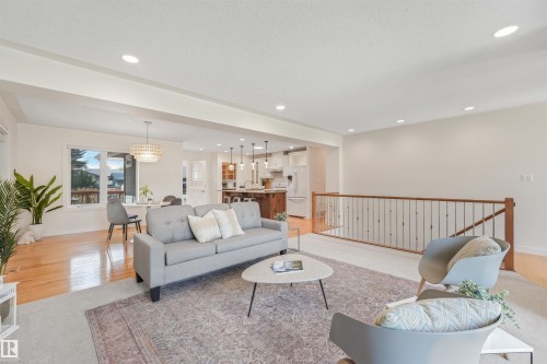 Open-concept living space featuring recessed lighting, wood-finish flooring, a contemporary chandelier, and a wood and metal railing - 8212 148 Street Nw, Edmonton, AB 