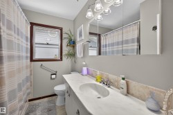 Bathroom featuring a single window with dark wood trim, a built-in vanity with a single sink, a tiled backsplash, and an overhead vanity light fixture - 