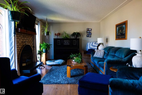 Brick fireplace with a dark metal surround, wood-finish flooring, and neutral wall paint - 11119 137 Avenue Nw, Edmonton, AB 