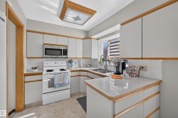 Kitchen featuring white cabinetry with wood-finish trim, stainless steel microwave, white electric range, and light-toned countertops - 