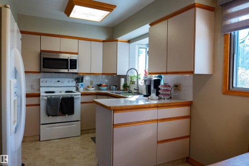 White tile backsplash, light wood-finish cabinetry, stainless steel microwave, and vinyl flooring - 11119 137 Avenue Nw, Edmonton, AB 