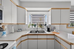 White cabinetry with wood-finish trim, dual basin stainless steel sink, white tiled backsplash, and light-toned countertops - 