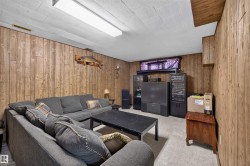 Finished basement recreation room featuring wood-paneled walls, drop ceiling with recessed lighting, carpeted flooring, and built-in entertainment cabinetry with media components - 