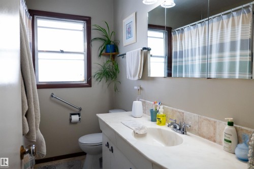 Bathroom with a vanity featuring an integrated sink and light-colored countertop, a wall-mounted mirror, and a window with dark trim - 11119 137 Avenue Nw, Edmonton, AB 