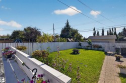 Private backyard featuring a white picket fence, a manicured lawn, a brick paver pathway, and a built-in fire pit - 