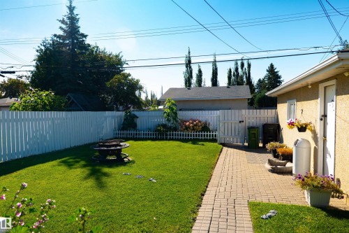 Manicured lawn with a white picket fence, brick paver patio, and exterior door access - 11119 137 Avenue Nw, Edmonton, AB 