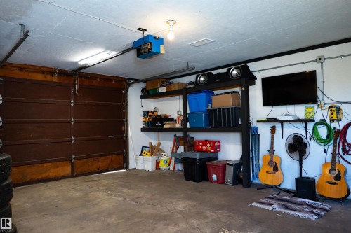Single-bay garage featuring a sectional overhead door with an automatic opener, exposed overhead lighting, and built-in wall shelving - 11119 137 Avenue Nw, Edmonton, AB 